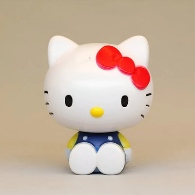 Figurine Hello Kitty blanche avec nœud rouge, nez jaune et salopette bleue
